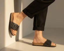 Ženske anatomske natikače od crne kože sa zlatnim uzorkom na nogama modela.